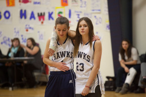 two girl basketball players, one in a cast with her arm around the other