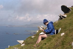 Woman sketching on a hill overlooking ocean