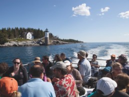 people on a boat riding by a lighthouse