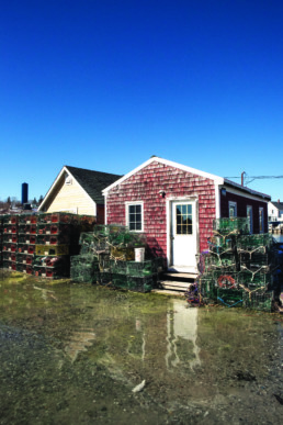 ocean water reaching the doorsteps of a red shack with lobster traps in front of it