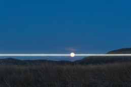 landscape art installation, line of light along horizon, striking through full moon